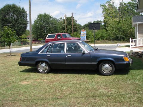 1985 Ford LTD - A dark blue 1985 Ford LTD sedan is parked on a grassy lawn with a red SUV in the background.