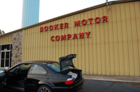 2002 BMW M3 - A black coupe is parked outside Booker Motor Company, with its trunk open, revealing some items inside.