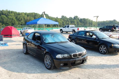 2002 BMW M3 - A black 2002 BMW M3 coupe is parked at a track event with tents and other vehicles nearby.