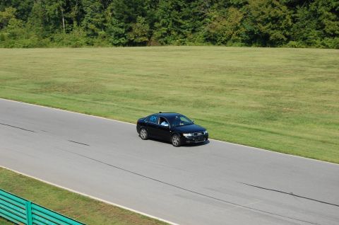 2002 BMW M3 - A black sedan is captured on a racetrack, with a wooded area and grassy field visible beyond the track.