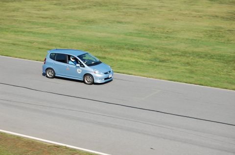 2002 BMW M3 - A blue Honda Fit is on a race track with a driver wearing a helmet.