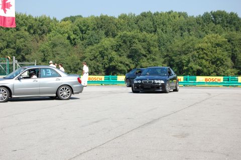 2002 BMW M3 - A black BMW M3 is on a race track, with a silver Subaru WRX in the foreground.