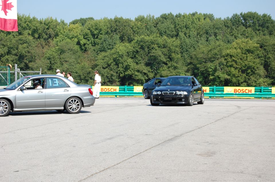 Black BMW M3 with front damage on a race track, viewed from the front-right