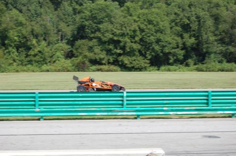 2002 BMW M3 - An orange Ariel Atom race car is seen on the track during a sunny day.