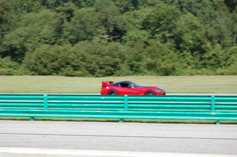 2002 BMW M3 - A red sports car drives along a racetrack with a green barrier in the foreground.