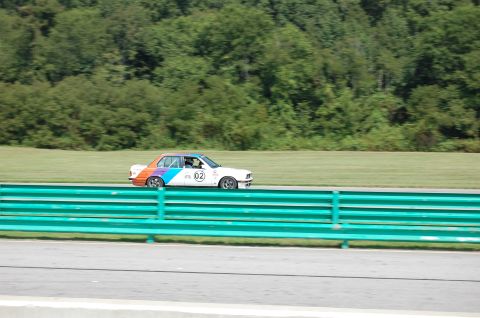 2002 BMW M3 - A race car with distinctive orange, blue, and purple stripes speeds along the track, displaying the number 02.