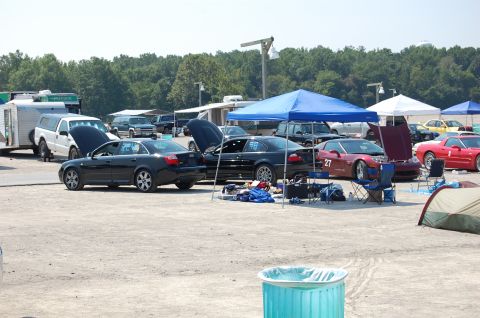 2002 BMW M3 - Cars and tents set up in a race track paddock area on a sunny day.