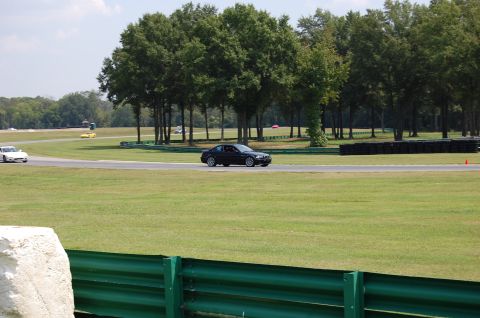 2002 BMW M3 - A black coupe drives on a race track with trees in the background and another car on the left.