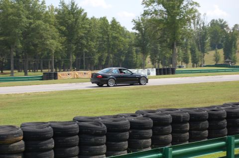 2002 BMW M3 - Black 2002 BMW M3 coupe driving on a race track with trees and tire barriers in the background.