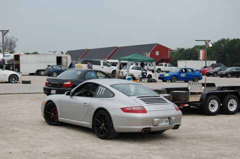 2002 BMW M3 - A silver Porsche 911 is parked on a dirt lot with other vehicles and trailers in the background.