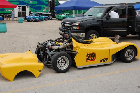 2002 BMW M3 - A yellow race car, number 29, with its front body panel removed, sits next to a pickup truck.