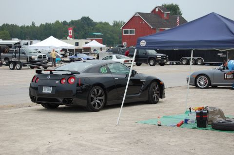 2002 BMW M3 - A black Nissan GT-R is parked on a dusty surface, with tents and other vehicles visible in the background.