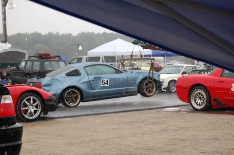 2002 BMW M3 - A blue Ford Mustang is being lifted by a crane on a rainy day at a race track.