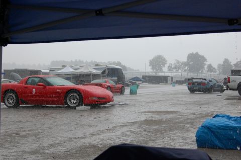 2002 BMW M3 - Several cars, including a red Corvette and a blue Mustang, are parked on a wet track during a rain shower.