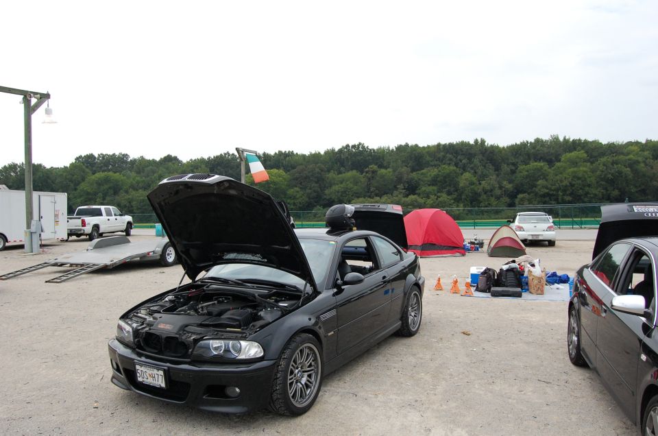 Black 2002 BMW M3 with hood open, parked at a track with tents and other cars around