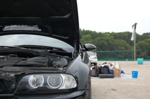 2002 BMW M3 - A black BMW M3 with its hood open is parked outdoors, with a white car and various items scattered on the ground behind it.