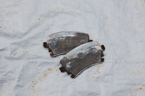 2002 BMW M3 - A pair of used brake pads are shown on a white cloth, with the Supermotors.net logo in the lower right corner.