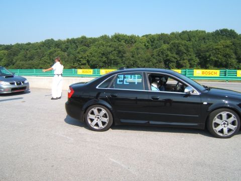 2002 BMW M3 - A black sedan with blue racing numbers on its window is parked on a race track next to another car.