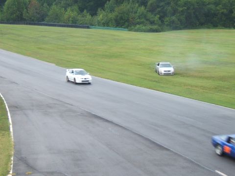 2002 BMW M3 - Two cars are on a racetrack, one is on the asphalt and the other is on the grass.