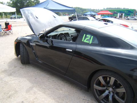 2002 BMW M3 - A black sports car, possibly a Nissan GT-R, is parked with its hood open, displaying the number 121 on the driver's side window.
