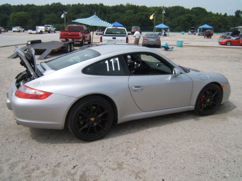 2002 BMW M3 - Silver Porsche 911 with racing numbers on the door and open trunk at a track event.