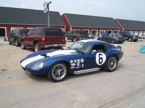 2002 BMW M3 - A blue Shelby Daytona Coupe replica with racing stripes and number 6 is parked on asphalt, with other vehicles and buildings in the backgro…
