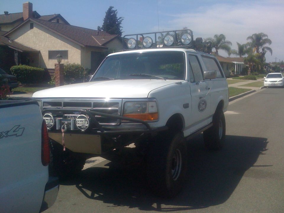 White Ford Bronco with off-road bumper, light bar, and large tires parked on a street