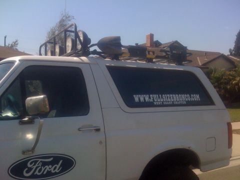 1995 Ford Bronco - White 1995 Ford Bronco with a roof rack, shovel, and lights is parked outdoors. It has a Ford logo and a website sticker.