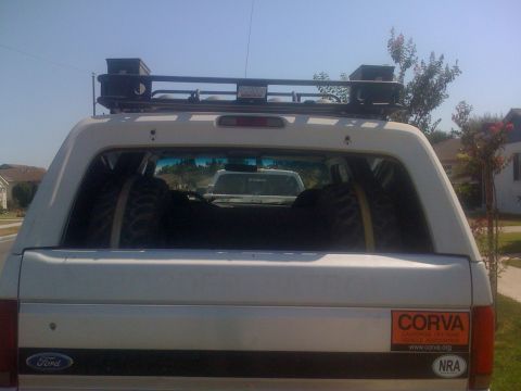 1995 Ford Bronco - This SUV has a roof rack and spare tires loaded inside, with another vehicle seen through the rear window.
