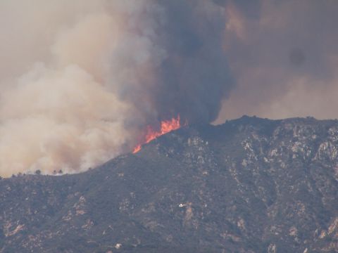 1990 Ford Bronco - A helicopter flies near a mountain engulfed in flames and smoke.