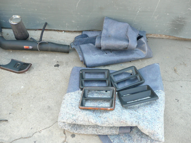 Black interior trim bezels and exhaust part with cone filter laid out on carpet and concrete