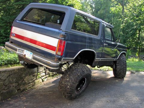 1986 Ford Bronco - This lifted Ford Bronco is positioned with its rear wheels on a stone wall, its off-road capabilities.