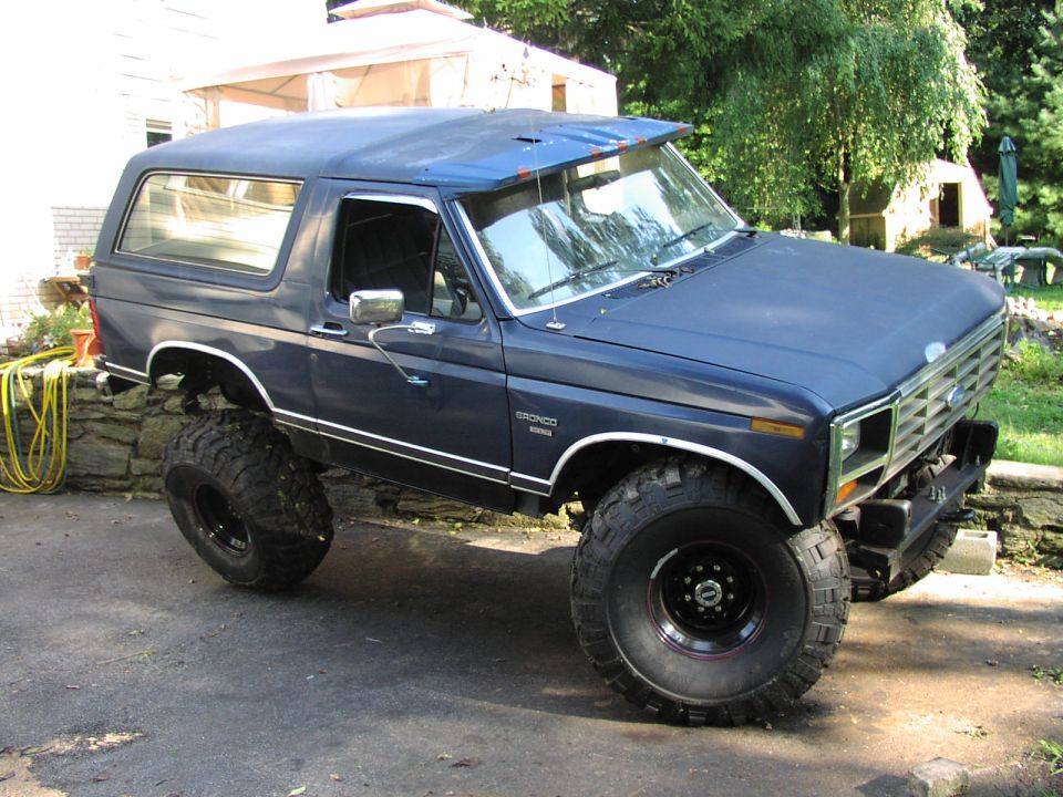 Blue Ford Bronco with lifted suspension and large tires, parked on asphalt