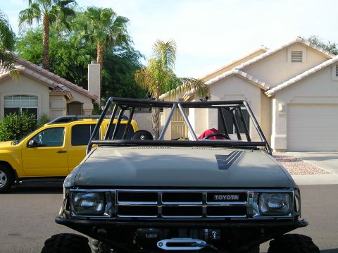 1986 Toyota Hilux - Modified Toyota pickup truck with a roll cage, seen from the front. A yellow SUV is parked nearby.