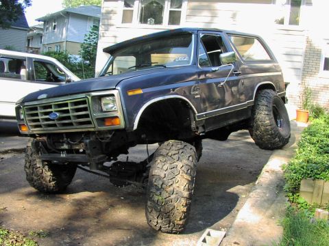 1986 Ford Bronco - This lifted 1980s Ford Bronco features oversized off-road tires and a prominent front grille, seen here in a 3/4 front view.