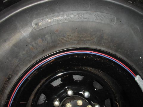 1986 Ford Bronco - A close-up view of a large off-road tire mounted on a black steel wheel with colored trim.