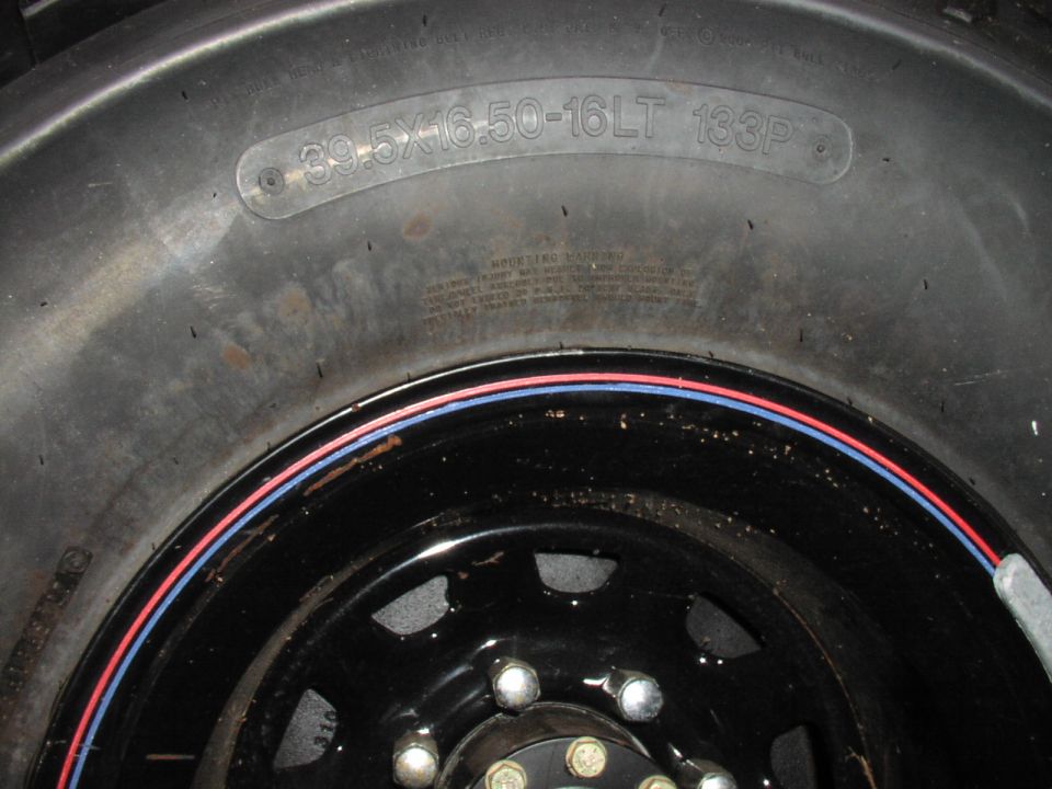 Close-up of a tire with size 39.5x16.50-16LT 133P and a black wheel with red and blue trim