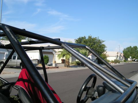 1986 Toyota Hilux - Interior view of a custom vehicle's roll cage and steering wheel, with a pickup truck parked on the street.