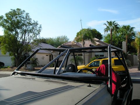 1986 Toyota Hilux - This custom off-road vehicle features an extensive roll cage, obscuring much of the interior. A yellow SUV is parked behind it.