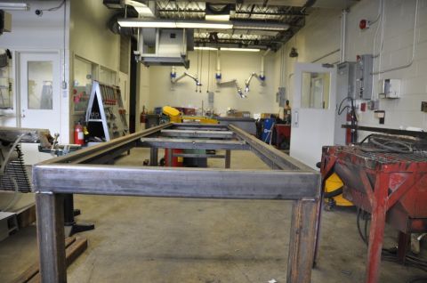 1996 Ford Bronco - A metal table frame is the focus in a workshop environment, with various tools and machinery visible.
