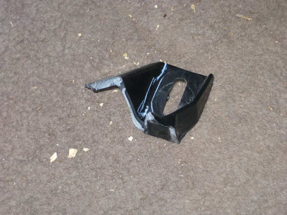 Black metal bracket with a hole, sitting on a carpeted surface