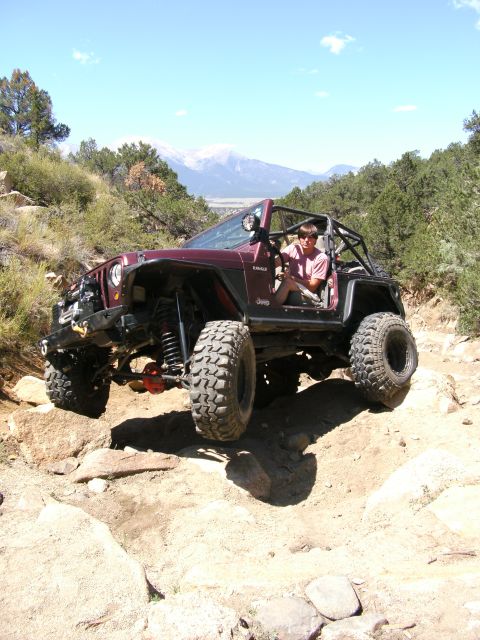 1995 Ford Bronco - A person drives a modified Jeep Wrangler over a rocky terrain with mountains in the background.