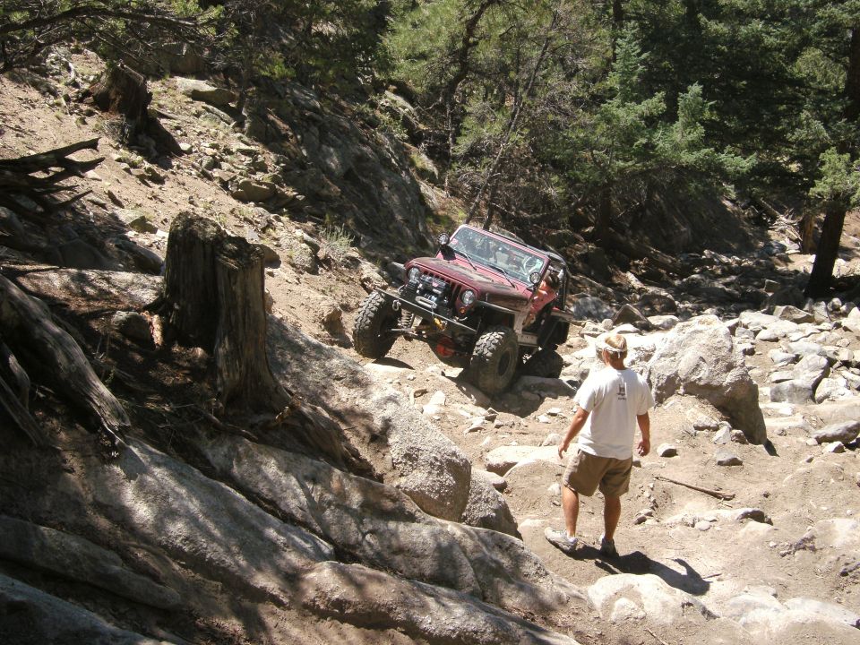 Red Jeep Wrangler navigating a steep, rocky trail with a person watching