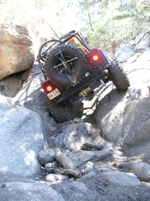 1995 Ford Bronco - This modified Jeep is navigating a difficult rocky terrain, with a person visible in the background.