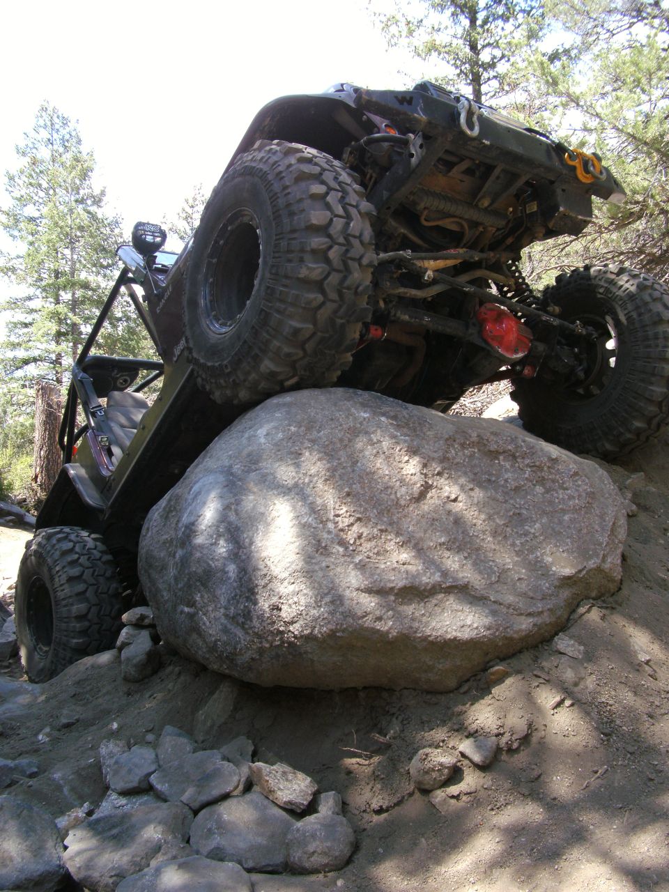 Off-road vehicle with large tires climbing over a boulder on a dirt trail