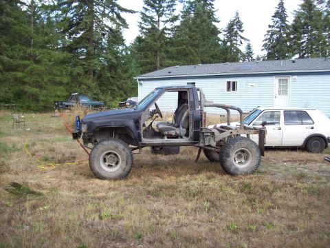 1985 Toyota Pickup/SR5 - This heavily modified pickup truck is missing its doors and body panels, sitting in a yard with a white car nearby.