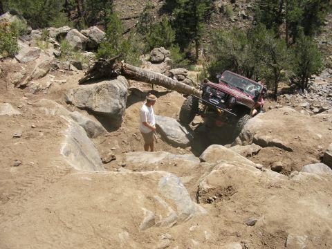 1995 Ford Bronco - Jeep Wrangler tackling a challenging rock crawl on a steep, sandy trail.