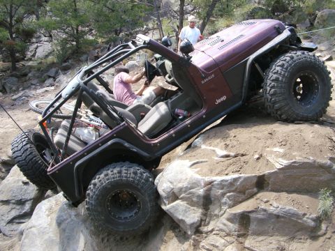 1995 Ford Bronco - A Jeep Wrangler navigates a difficult rocky terrain with two people inside.
