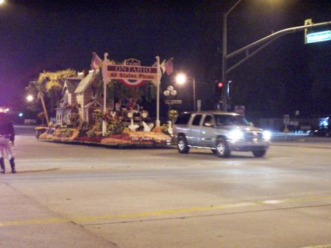 1990 Ford Bronco - A silver SUV drives past a parade float at night.