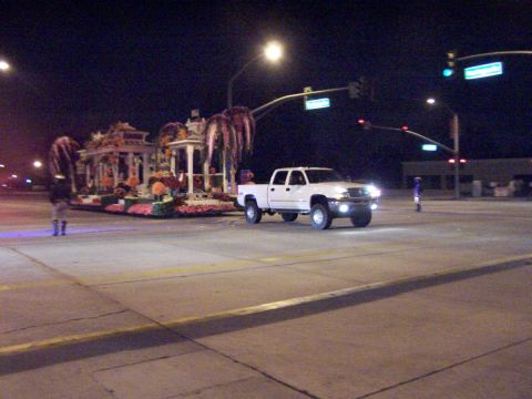1990 Ford Bronco - A white pickup truck passes a large, illuminated parade float on a city street at night.